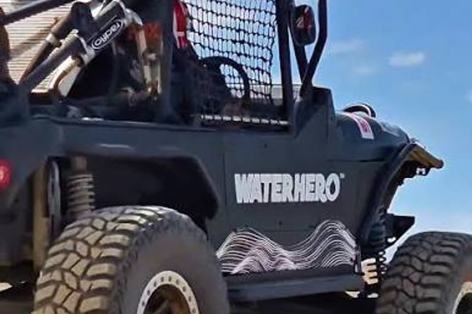 A caged off-road rock buggy on big mud tyres under a blue sky.